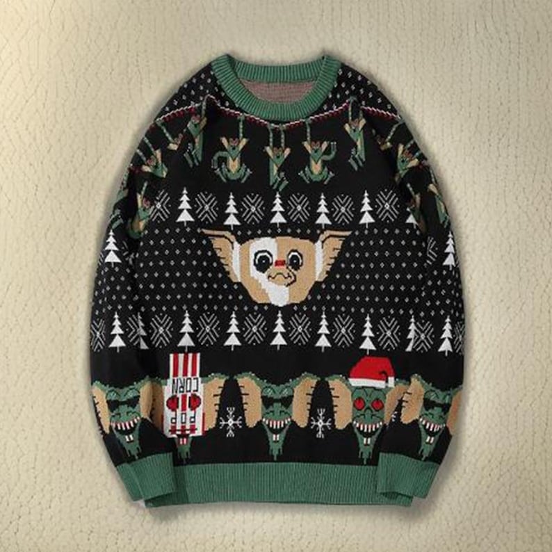 May include: Black Christmas sweater with a green and white pattern. The sweater features a graphic of a creature from the movie Gremlins, with the text "Pop Corn" on a red and white striped box.