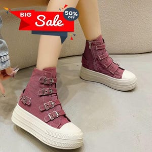 May include: High-top burgundy sneakers with multiple silver buckles and a white rubber sole. The sneakers have a side zipper and a white toe cap. The image also includes the text "BIG Sale 50% OFF".