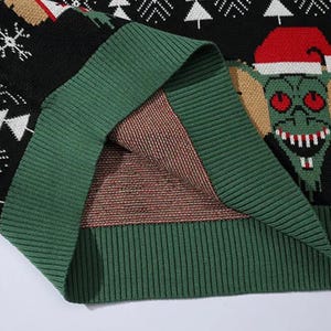 May include: Close-up of the green knit fabric on the inside of a black Christmas sweater with a green and white Christmas tree pattern and a green creature with red eyes wearing a Santa hat.