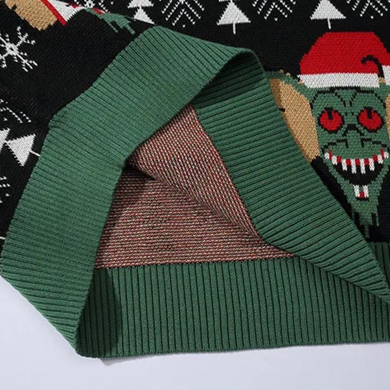 May include: Close-up of the green knit fabric on the inside of a black Christmas sweater with a green and white Christmas tree pattern and a green creature with red eyes wearing a Santa hat.