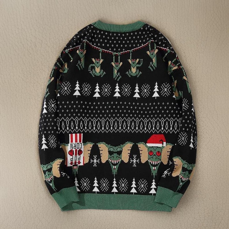 May include: Black Christmas sweater with a green, white, and red pattern. The sweater features a graphic of a creature from the movie 'Gremlins' with the text 'Corn' and 'Pop' on a red and white striped box.