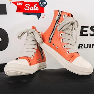 May include: Orange high-top sneakers with white soles and toe caps. The sneakers have gray laces, black zippers, and metal eyelets. The image includes a "Big Sale" banner with a 50% off tag.
