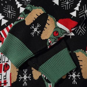 May include: A black and green Christmas sweater with a white snowflake pattern and a green creature wearing a Santa hat. The sweater has a green and black ribbed cuff.