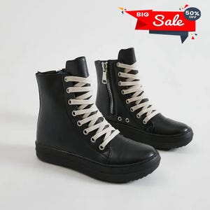 May include: A pair of black high-top sneakers with cream-colored laces and a side zipper. The shoes have a thick, black sole and are displayed against a white background. A red and white "Sale" banner is in the top right corner.