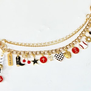 May include: Gold-toned keychain with multiple charms. Charms include a black cowboy boot, a baseball, a cross, a star, and a heart. The keychain also has the word "Amen" and the text "LET'S GO".