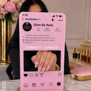 May include: A pink acrylic social media profile display stand featuring the Glam By Nails account interface. The screen displays profile details, including 95 posts, 8,750 followers, and 210 following, with a cutout window showcasing manicured nails.