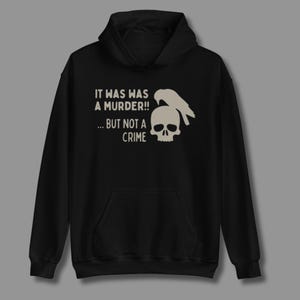 Puede incluir: Sudadera con capucha negra con un gráfico blanco de una calavera y un pájaro, con el texto "IT WAS A MURDER!! ... BUT NOT A CRIME". La sudadera tiene un bolsillo delantero y una capucha con cordón.