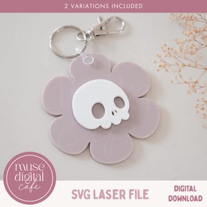 May include: A lilac flower-shaped keyring with a white skull emblem. The keyring has a silver-coloured clasp and a ring for keys. The image includes the text "2 VARIATIONS INCLUDED", "SVG LASER FILE", and "DIGITAL DOWNLOAD".