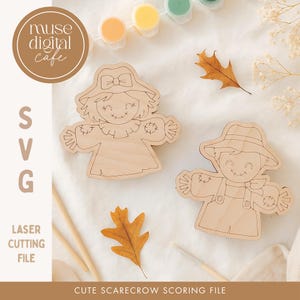 May include: Two wooden scarecrow cutouts with smiling faces, one wearing a hat with a bow and the other a straw hat. The image includes paint pots, a paintbrush, and fall leaves. Text reads "muse digital cafe", "SVG", "laser cutting file", and "cute scarecrow scoring file."