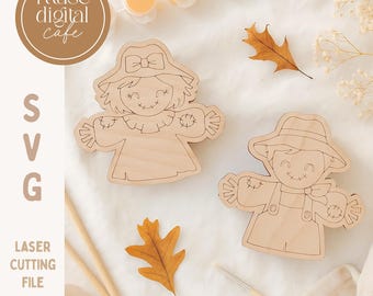 May include: Two wooden scarecrow cutouts with smiling faces, one wearing a hat with a bow and the other a straw hat. The image includes paint pots, a paintbrush, and fall leaves. Text reads "muse digital cafe", "SVG", "laser cutting file", and "cute scarecrow scoring file."