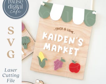 May include: Wooden sign for "Kaiden's Market" with a green and white awning design. The sign features the text "Fresh & Local" and the name "Kaiden's Market" in white letters. Includes colorful fruit and vegetable designs: corn, grapes, and an apple.