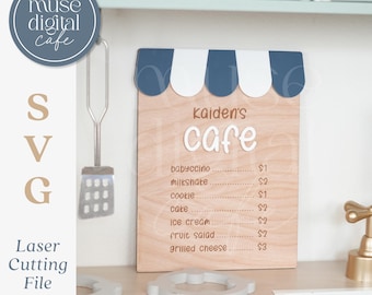 May include: A wooden sign for "Kaiden's Cafe" with a blue and white awning design. The menu includes items like babyccino, milkshake, and ice cream. The sign is a laser cutting file.