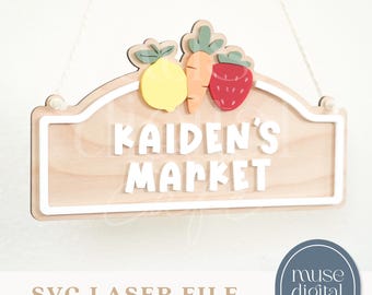 May include: Wooden sign with the text "KAIDEN'S MARKET" in white, topped with a lemon, carrot, and strawberry. The sign is light brown with a white border and is hanging by a white string. The words "SVG LASER FILE" and "digital download" are at the bottom.
