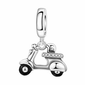 Puede incluir: Un charm de plata con un diseño de scooter. El scooter tiene ruedas negras y un casco con una fila de piedras transparentes. El charm tiene un lazo en la parte superior para sujetarlo a una pulsera o collar.