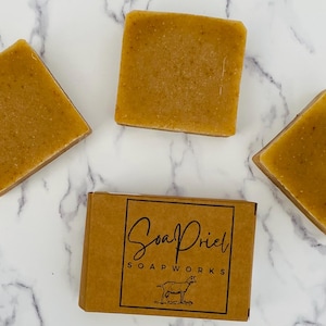 May include: Three bars of handmade soap with a light brown color. The soap is labeled "Soapriel Soapworks".