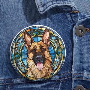 May include: A round button featuring a German Shepherd dog with a stained-glass style background. The dog has brown and tan fur, with its tongue sticking out. The background is a mix of blue, yellow, and green.