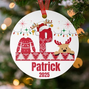 May include: A white Christmas ornament with a red ribbon. The ornament features a red letter "P" with a reindeer wearing a Santa hat, a red sweater design, and the name "Patrick" and the year "2025" in red text.