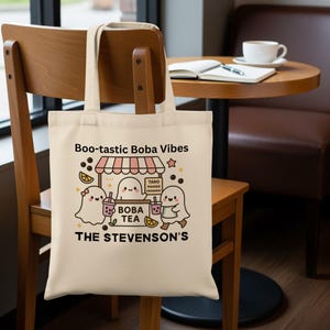 May include: Cream-colored tote bag with the text "Boo-tastic Boba Vibes" and a cartoon illustration of ghosts at a boba tea stand. The bag features the text "THE STEVENSON'S" below the illustration.