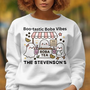 May include: White sweatshirt with a colorful graphic. The design features ghost characters, boba tea, and the text "Boo-tastic Boba Vibes" and "The Stevenson's". The design includes a boba tea stand.