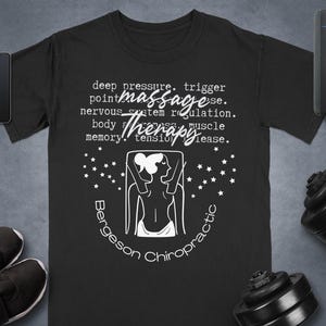 May include: Black t-shirt with white text and a graphic related to massage therapy. The text includes "deep pressure," "massage," and "therapy." A drawing of a person is in the center, with the words "Bergeson Chiropractic" below.
