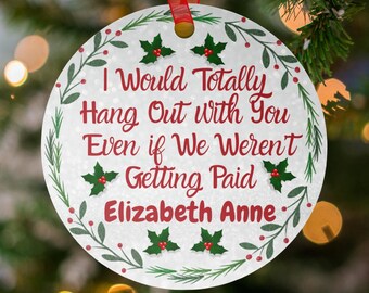 May include: A round white Christmas ornament with a red ribbon hanger, featuring a green holly and berry wreath border. The text reads: I Would Totally Hang Out With You Even if We Weren't Getting Paid, followed by the name Elizabeth Anne.
