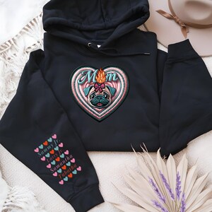 Könnte beinhalten: Schwarzer Hoodie mit einem herzförmigen Design, das einen Mops mit einer Flamme auf dem Kopf und dem Wort "Mom" im Herzen zeigt. Der Ärmel hat eine vertikale Reihe von Herzen mit den Namen Sammy Jr., Larry Jr., Samantha und Tabatha, die darin gedruckt sind.