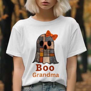 以下が含まれることがあります： オレンジ色のリボンが付いた、パッチワークのゴーストデザインの白いTシャツ。ゴーストは、グレー、オレンジ、茶色のさまざまな生地パターンで構成されています。「Boo Grandma」の文字が下にオレンジ色でプリントされています。