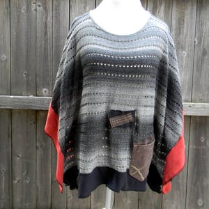 May include: A gray and black striped knitted poncho with red trim and a black lining. The poncho has two pockets on the front.