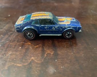 May include: A vintage blue toy car with a detailed orange and gold design on the roof and hood. The car has black wheels with red rims and shows signs of wear, adding to its classic appeal. This collectible toy car is a nostalgic item.