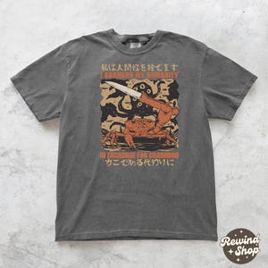 May include: Dark grey t-shirt featuring a graphic of a crab holding a knife, with an octopus and text that reads "I Abandon My Humanity In Exchange For Crabhood". The shirt has a vintage, distressed look.