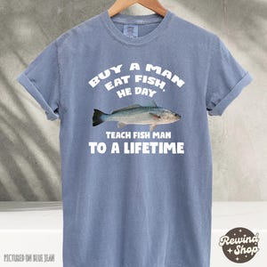 May include: A light blue t-shirt with the text "Buy a man eat fish, he day. Teach fish man to a lifetime." and a white silhouette of a fish.
