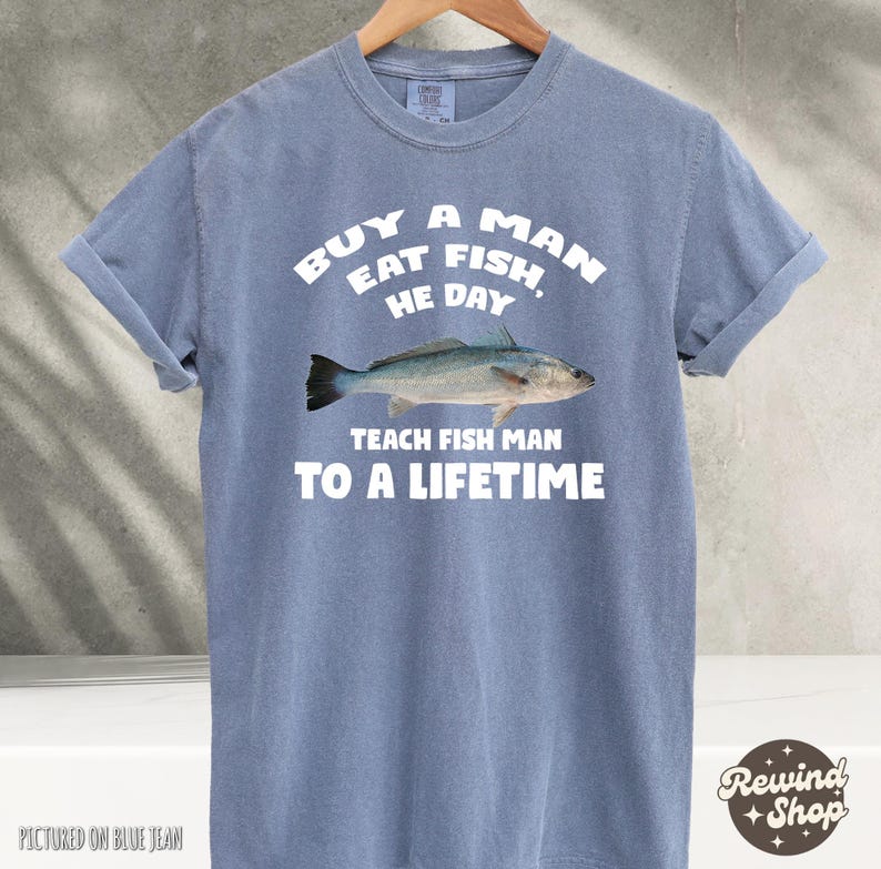 May include: A light blue t-shirt with the text "Buy a man eat fish, he day. Teach fish man to a lifetime." and a white silhouette of a fish.