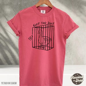 May include: A red t-shirt with a black graphic of a goose in a cage. The text "Got Too Silly" is above the graphic.
