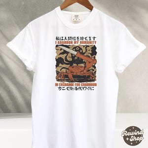 May include: White t-shirt with a graphic design featuring a crab holding a knife, with an octopus and text in English and Japanese. The text reads "I ABANDON MY HUMANITY" and "IN EXCHANGE FOR CRABHOOD".