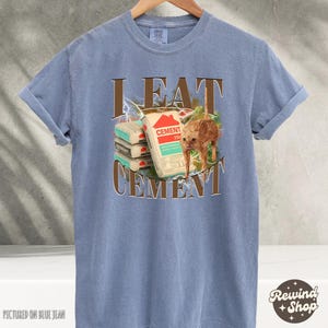 May include: A blue t-shirt with the text "I EAT CEMENT" in brown letters. A cartoon cat is eating a stack of cement bags.