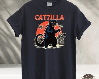 May include: Black t-shirt with a graphic of a black cat monster with red eyes, a city skyline, and the text "CATZILLA".
