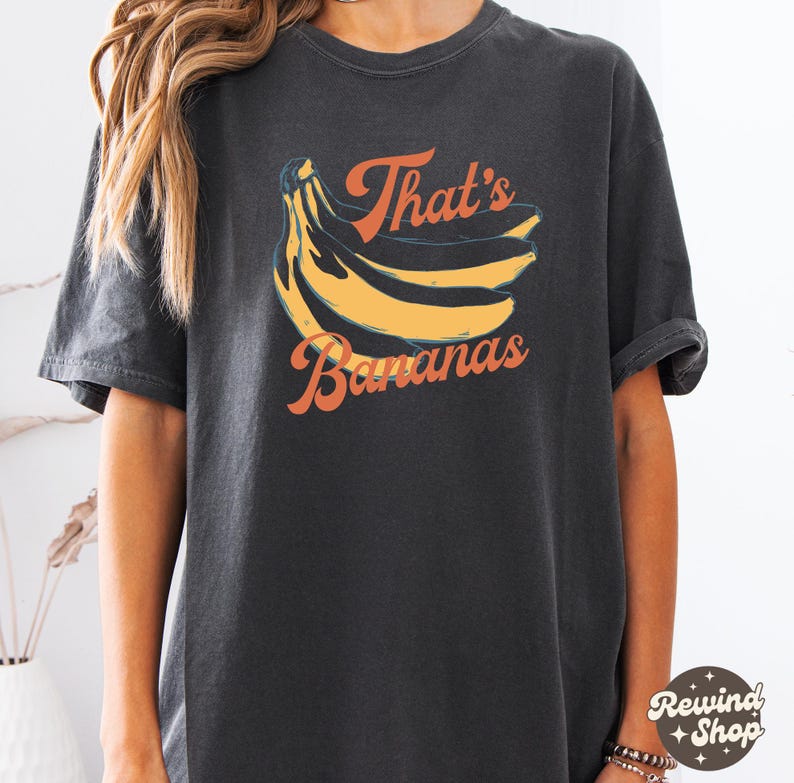 May include: Dark gray t-shirt featuring a graphic of yellow bananas and the text "That's Bananas" in orange. The shirt has a vintage, washed look and a relaxed fit, suitable for casual wear.