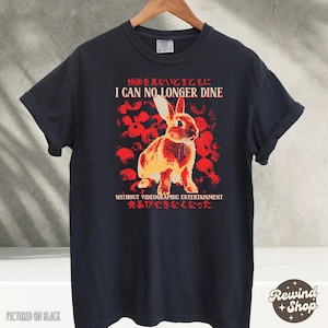 May include: Black t-shirt featuring a rabbit illustration with the text "I CAN NO LONGER DINE WITHOUT VIDEOGRAPHIC ENTERTAINMENT" in red and white. The design includes Japanese text and a red floral background.