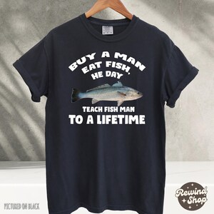 May include: A black t-shirt with white text that reads "Buy a man eat fish, he day teach fish man to a lifetime". The shirt features a graphic of a fish.