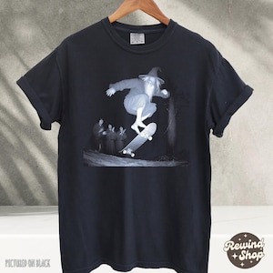 May include: Black t-shirt with a graphic of a wizard skateboarding. The wizard is wearing a pointed hat and a long beard. The graphic is in black and white. The text "Pictured on Black" is at the bottom of the image.