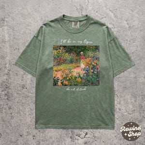 Puede incluir: Camiseta verde salvia con un estampado floral enmarcado. El estampado muestra una escena de jardín y el texto "I'll be in my Office" y "do not disturb". La camiseta tiene mangas cortas.