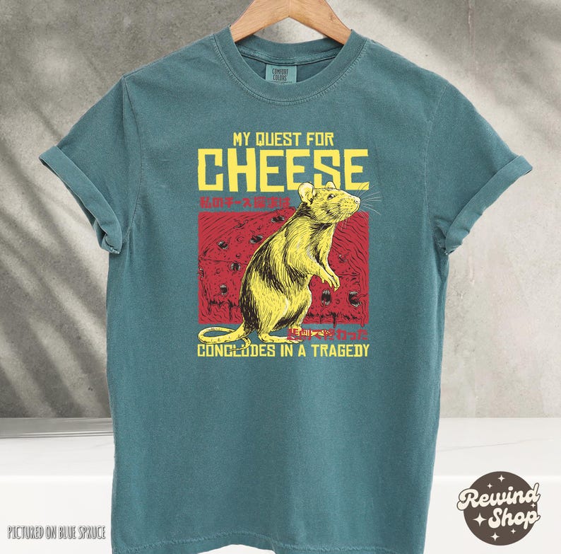 Op de afbeelding: Tealblauwe T-shirt met een afbeelding van een rat en de tekst "My Quest for Cheese Concludes in a Tragedy".