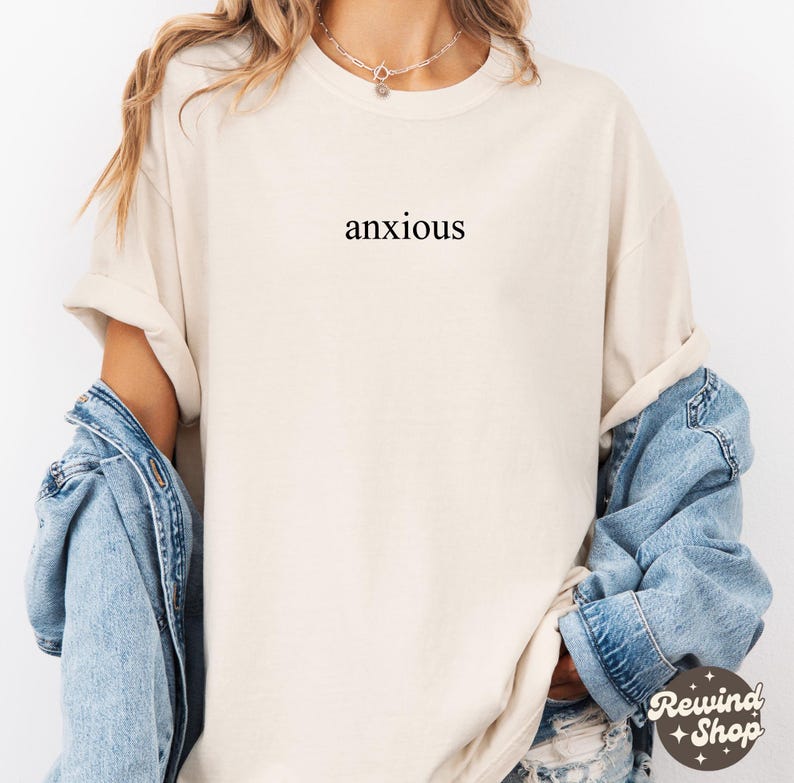 May include: A cream colored t-shirt with the word "anxious" printed in black on the front.