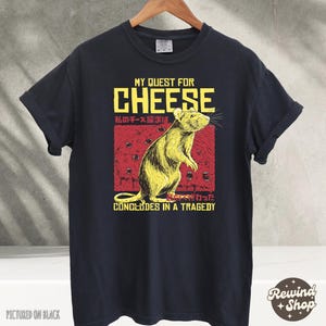 Op de afbeelding: Zwart T-shirt met een afbeelding van een rat en de tekst "My Quest for Cheese" in rood en geel. De tekst "私のチーズ探求は" is in het Japans en de tekst "CONCLUDES IN A TRAGEDY" is in zwart.
