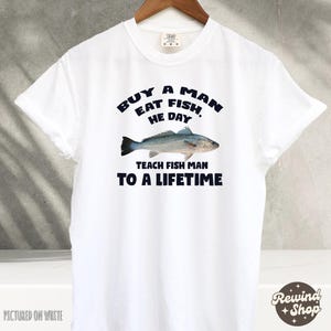 May include: White t-shirt with a blue graphic that says "Buy a man eat fish, he day teach fish man to a lifetime". The graphic also includes a drawing of a fish.