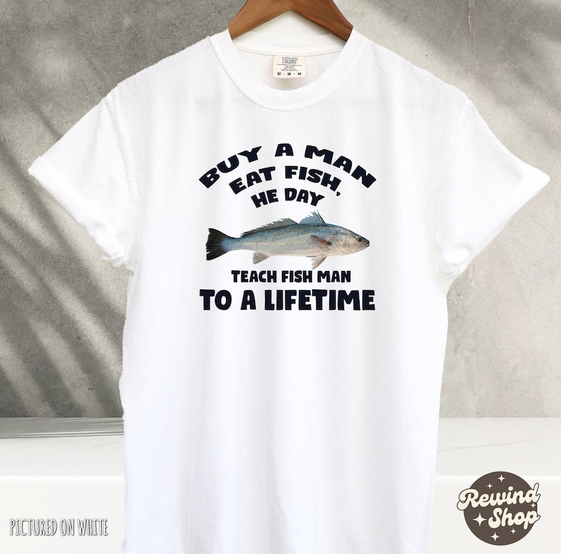May include: White t-shirt with a blue graphic that says "Buy a man eat fish, he day teach fish man to a lifetime". The graphic also includes a drawing of a fish.