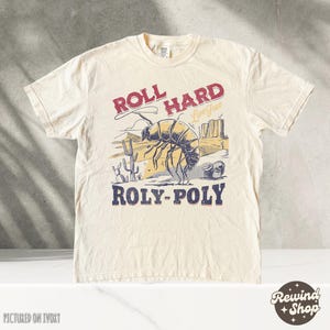 Puede incluir: Una camiseta de color crema con un gráfico de un bicho bolita y el texto "Roll Hard Live Free Roly-Poly".