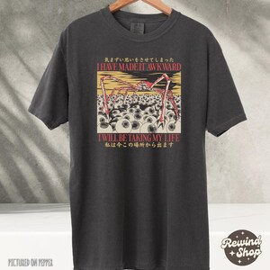 May include: Dark gray t-shirt featuring a graphic with a red and yellow spider-like creature above a field of white eyeballs. The text "I HAVE MADE IT AWKWARD" and "I WILL BE TAKING MY LIFE" are also displayed.