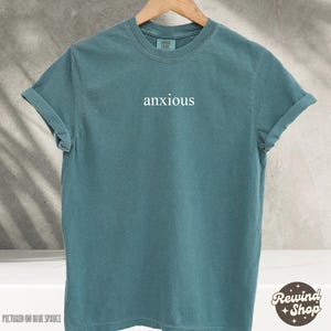 May include: A teal blue t-shirt with the word "anxious" printed in white on the front.