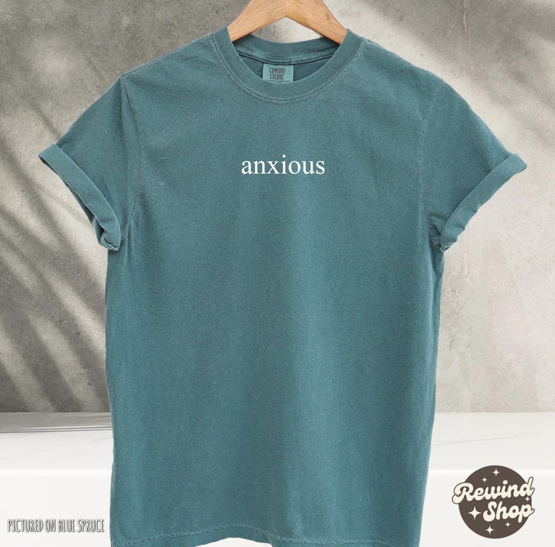 May include: A teal blue t-shirt with the word "anxious" printed in white on the front.